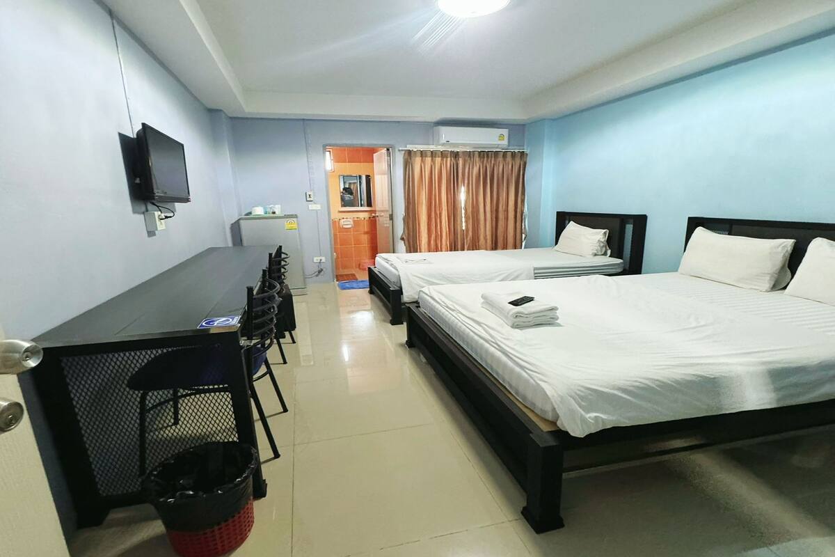 A hotel room with two beds, a desk, a TV, and a kitchenette.
