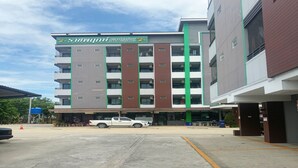A multi-story building with a green and brown facade, a visible water tank, and a parking area with a white pickup truck. - OYO 75506 Ratchapruek Apartment Suphanburi  (Suphan Buri)