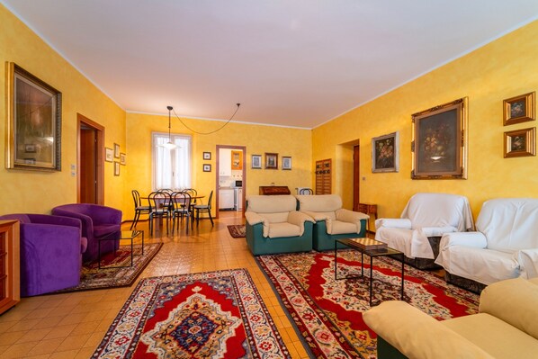 Een woonkamer met een zithoek, een eethoek met stoelen en een tafel, en een keuken op de achtergrond.
