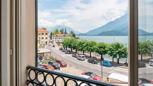 Une vue depuis une fenêtre donnant sur une rue où sont garées des voitures, avec des arbres et des bâtiments en arrière-plan.