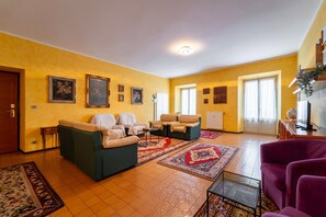 Een ruime woonkamer met een zithoek, een salontafel en een paarse fauteuil.