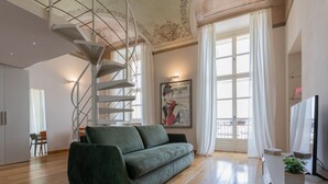 A modern living room with a spiral staircase, a green sofa, a flat-screen TV, and a large window with curtains. - La Casa del Mercato by Wonderful Italy (Turin)