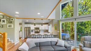 A modern living room with a gray sectional sofa, wooden flooring, and a dining area with a table and chairs. - Yellow Tail Cabin in Hoodsport (Hoodsport)