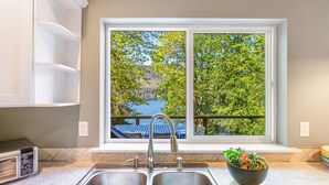 A kitchen with a double sink, a built-in microwave, and a window overlooking a lake and trees. - Yellow Tail Cabin in Hoodsport (Hoodsport)