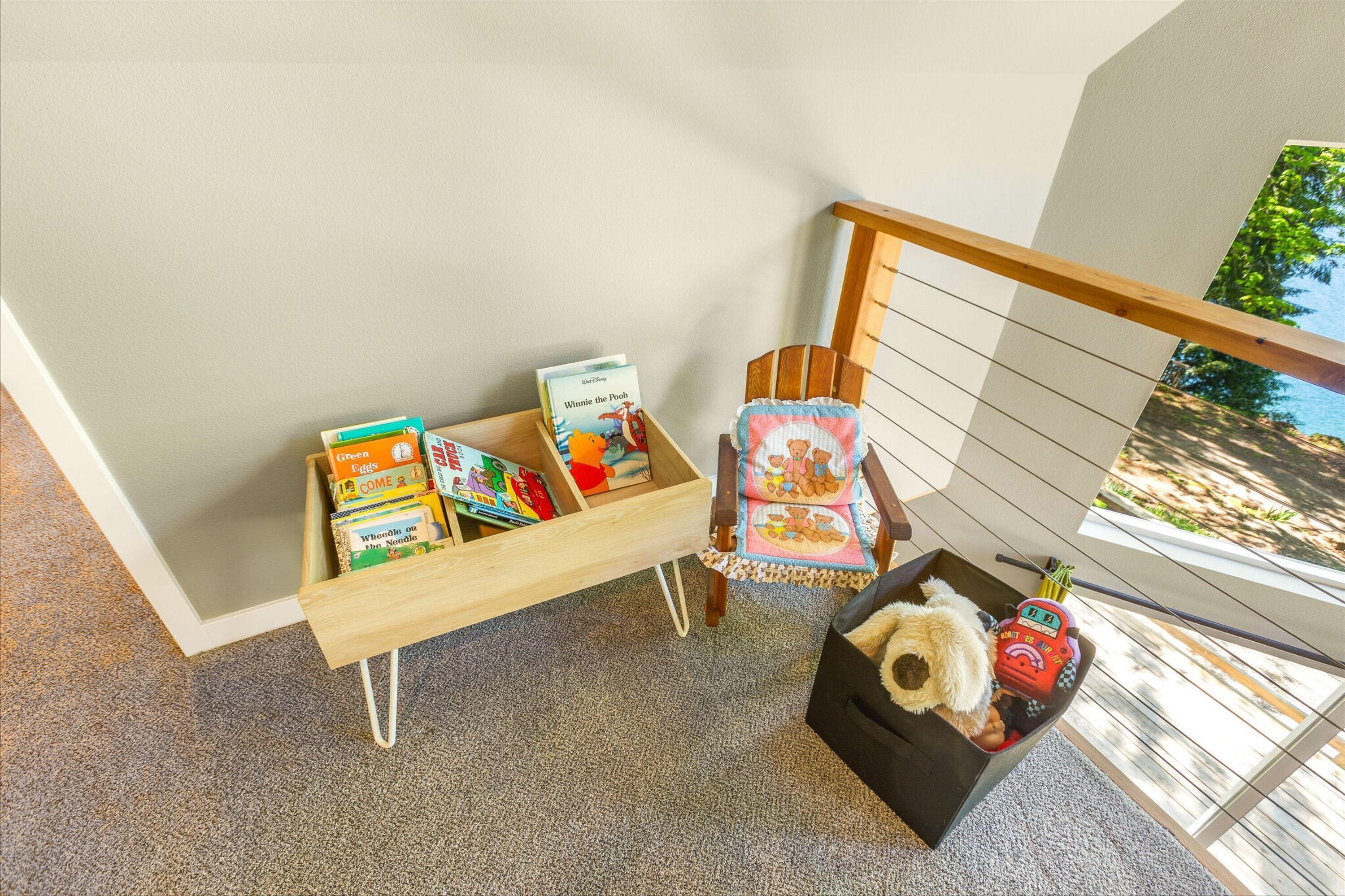 A child’s play area with a wooden bench holding books and toys, a cushioned chair with a Winnie the Pooh design, and a small table with a teddy bear and a toy car.