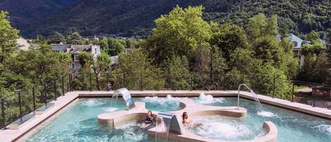 Piscina con múltiples jacuzzis y cascadas, rodeada de exuberante vegetación y montañas.