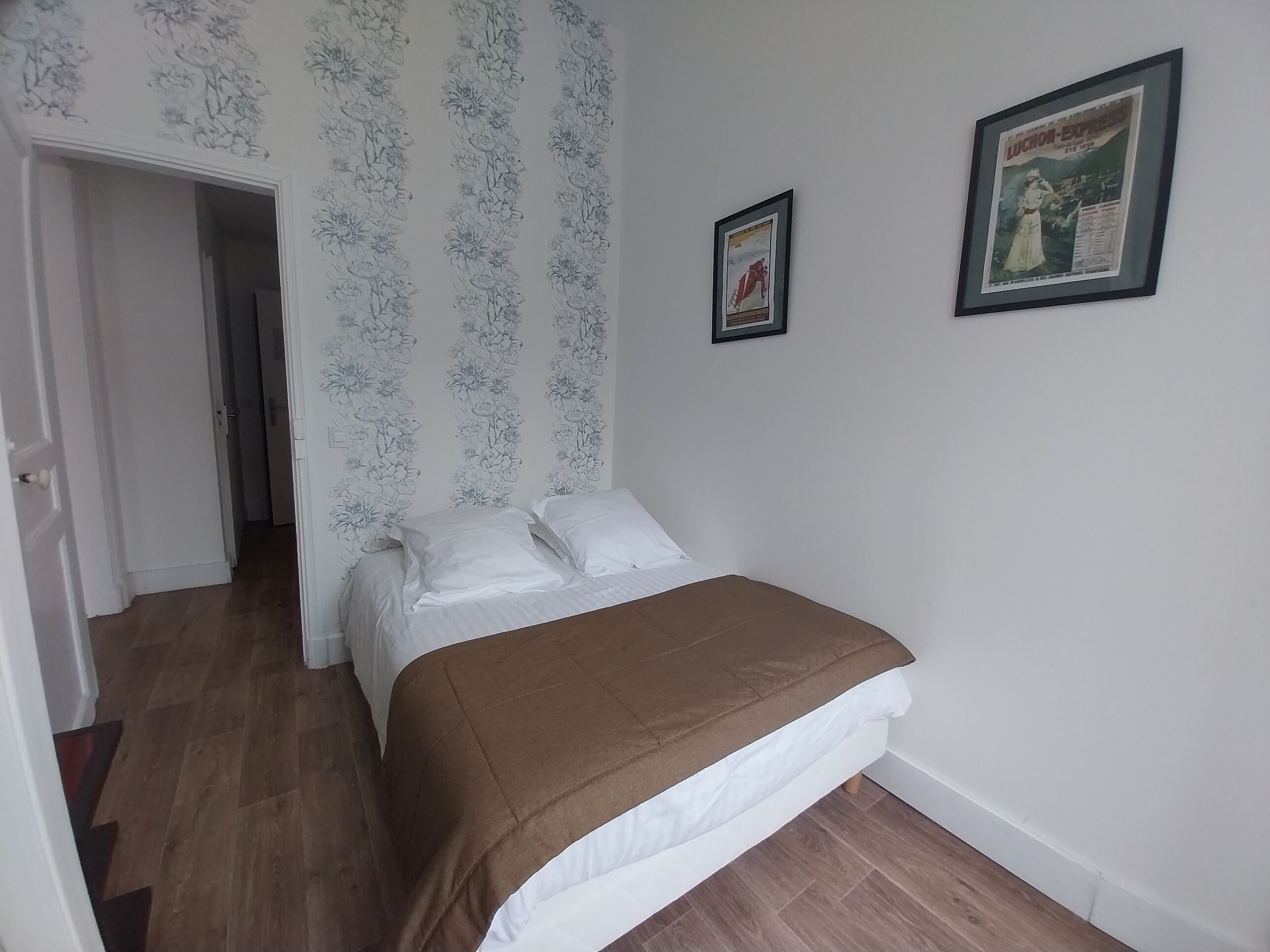 A bedroom with a bed, a door, a hallway, and a poster on the wall.