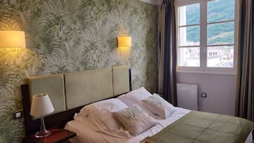Een hotelkamer met een bed, twee bedlampen, een raam met gordijnen en een muur met tropisch behang.
