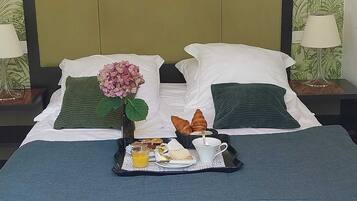 A neatly made bed with a tray of breakfast items, including croissants, cheese, and juice.
