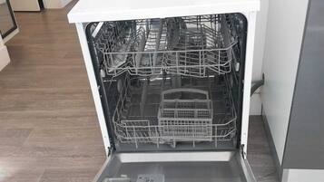 An open dishwasher with a microwave on top, a sink, and a tiled floor.
