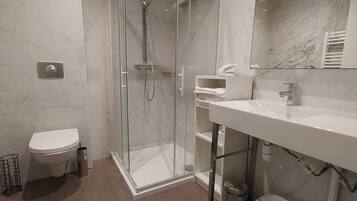 A modern bathroom with a glass-enclosed shower, a toilet, a sink, and a mirror.