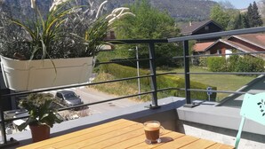 Een houten tafel met twee koffieglazen, een potplant en op de achtergrond huizen en bergen.