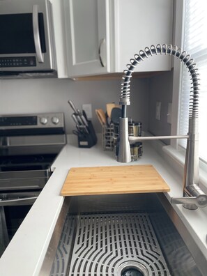A kitchen with a stainless steel sink, a wooden countertop, and a window with blinds.