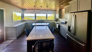 Una cocina moderna con una isla central, electrodomésticos integrados y grandes ventanales que ofrecen vistas al exterior.