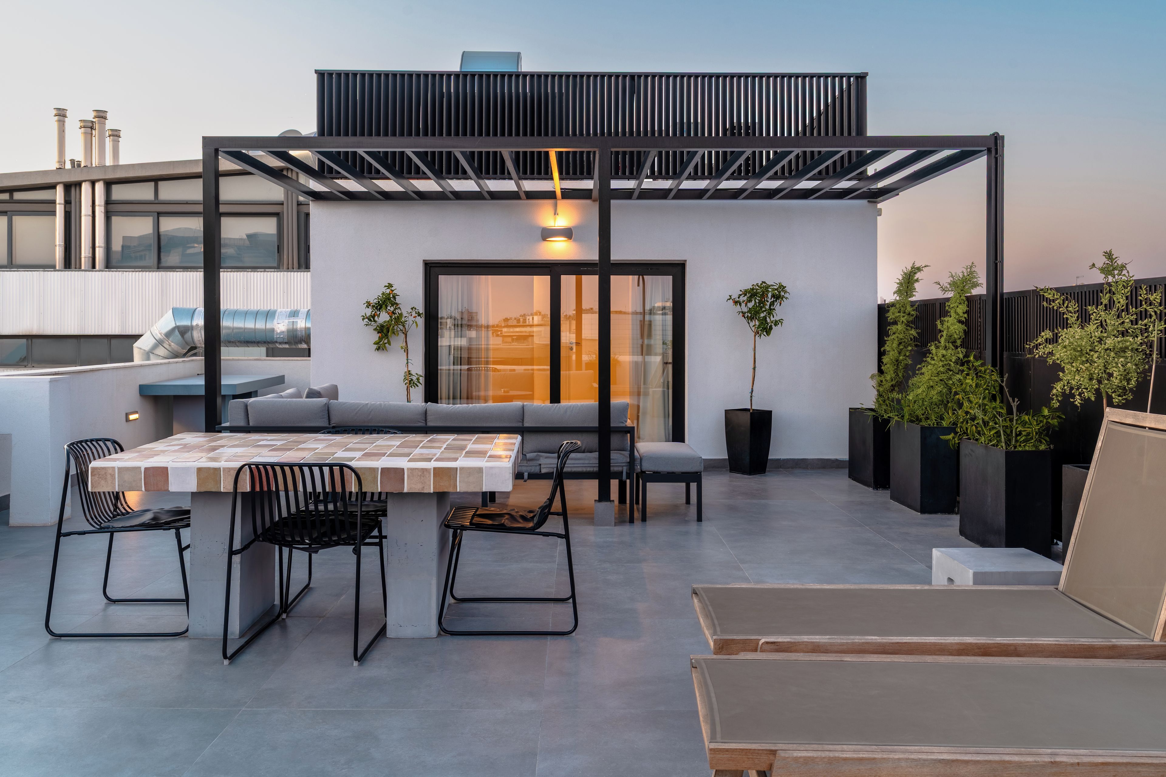 A rooftop terrace with a dining area, seating, and potted plants.