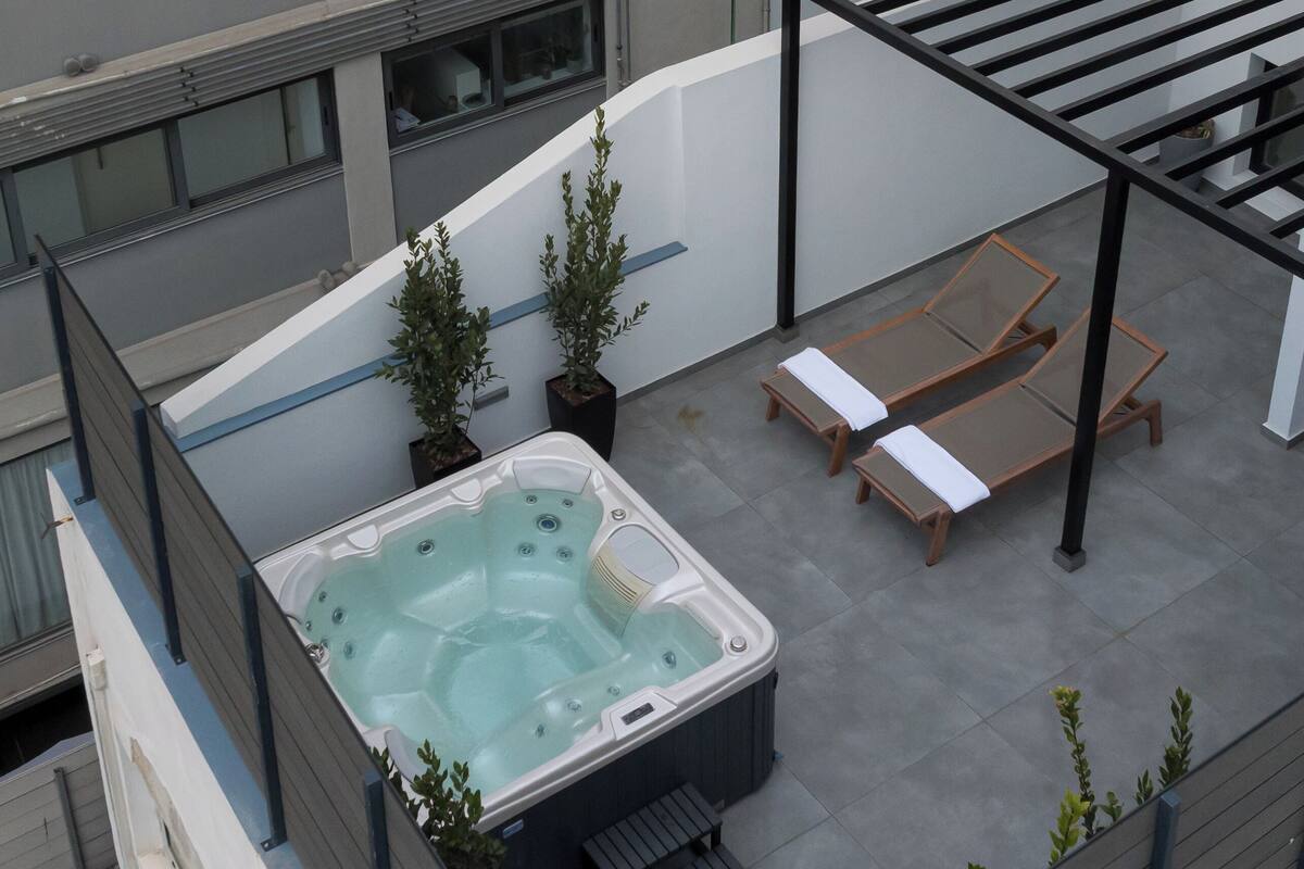 A rooftop patio with a hot tub, two lounge chairs, and potted plants.
