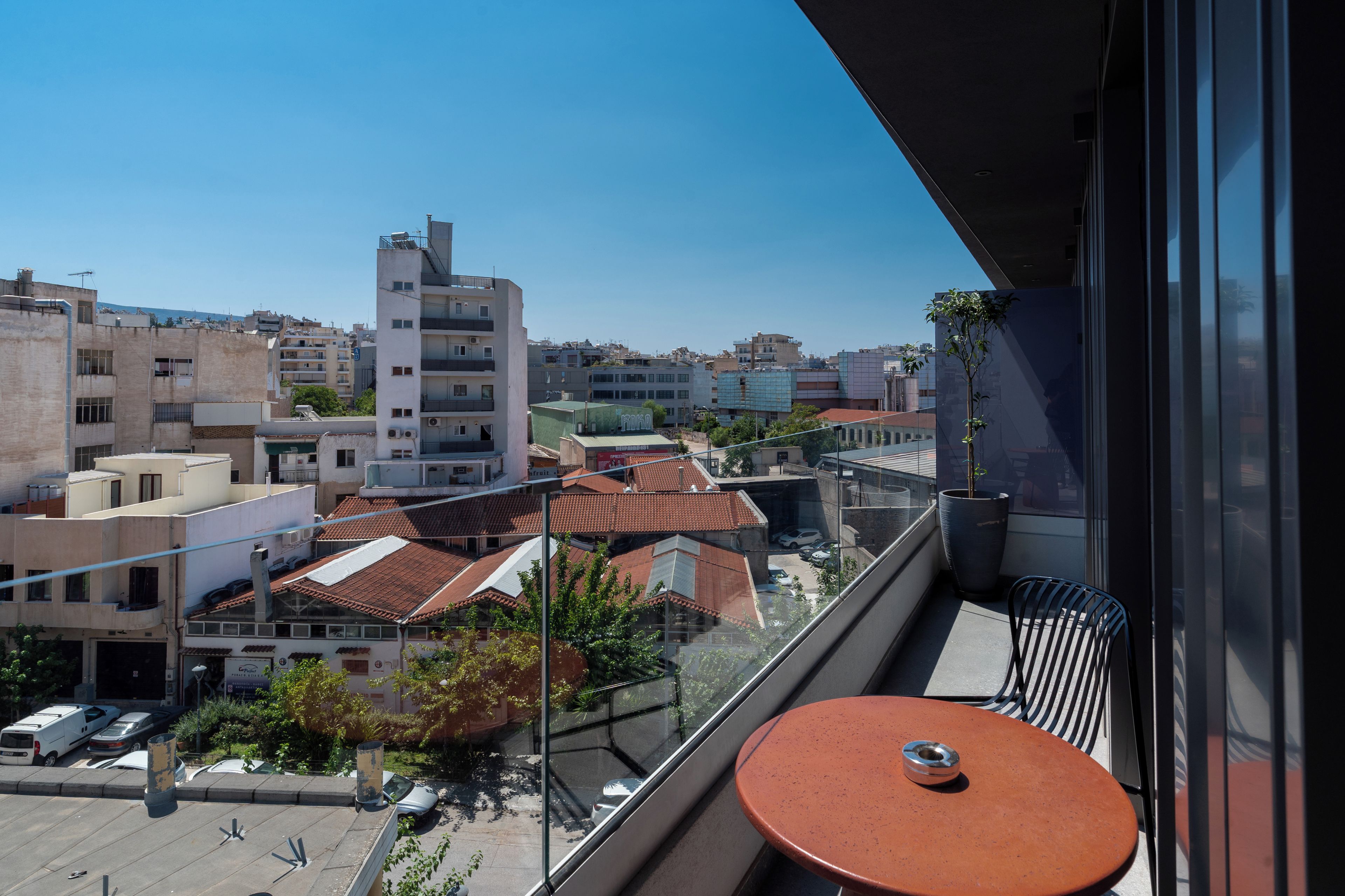 A balcony with a table and chairs, overlooking a cityscape with various buildings and a clear sky.