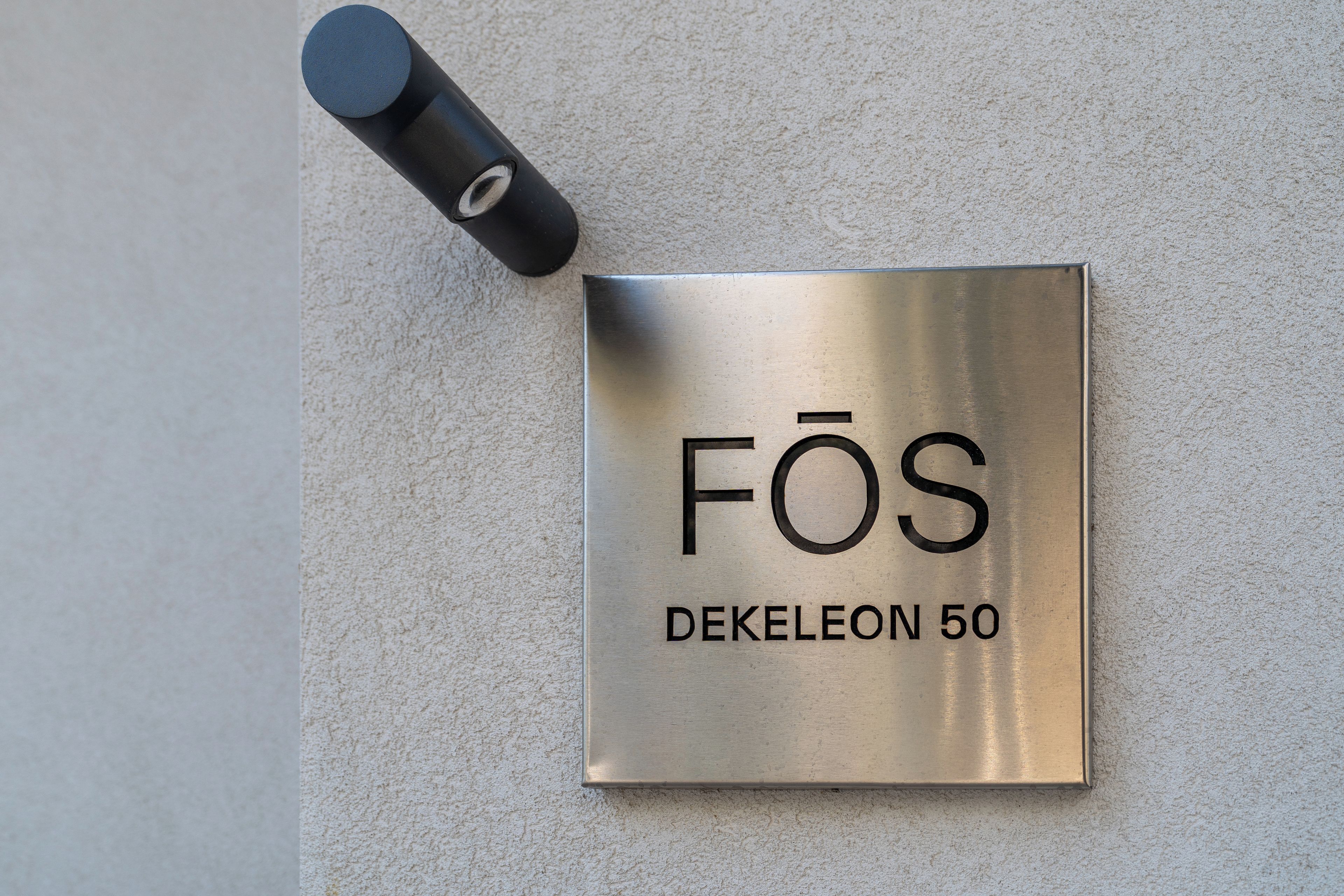 Una placa metálica con la inscripción 'FÖS DEKELEON 50' fijada en una pared con textura.