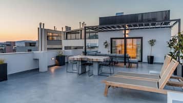 Una terraza en la azotea con zona de comedor, sillas de descanso y un pérgola.