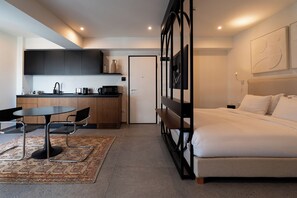 A modern hotel room with a bed, a desk, a kitchenette, and a bathroom. - Fos (Athens)