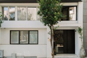 A two-story building with large windows and a tree in front. - Fos (Athens)
