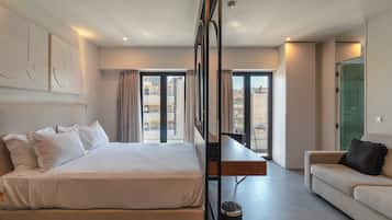 Habitación de hotel con cama, sofá, escritorio y vistas a la ciudad a través de amplias ventanas.