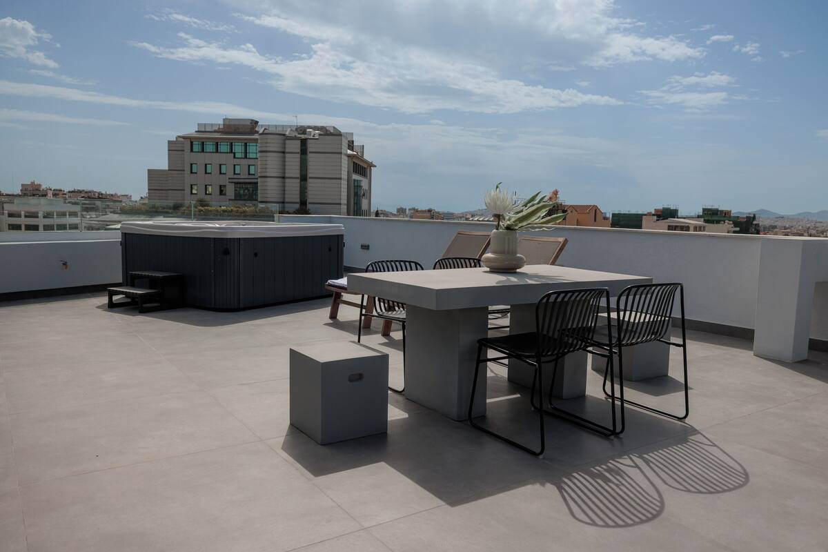 A rooftop terrace with a table and chairs, a small seating area, and a view of the cityscape.
