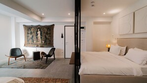 A modern bedroom with a large bed, two chairs, a tapestry, and a door. - Fos (Athens)