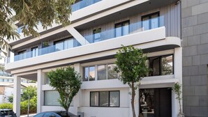 A modern multi-story building with balconies, a car parked in front, and a potted plant on the sidewalk. - Fos (Athens)
