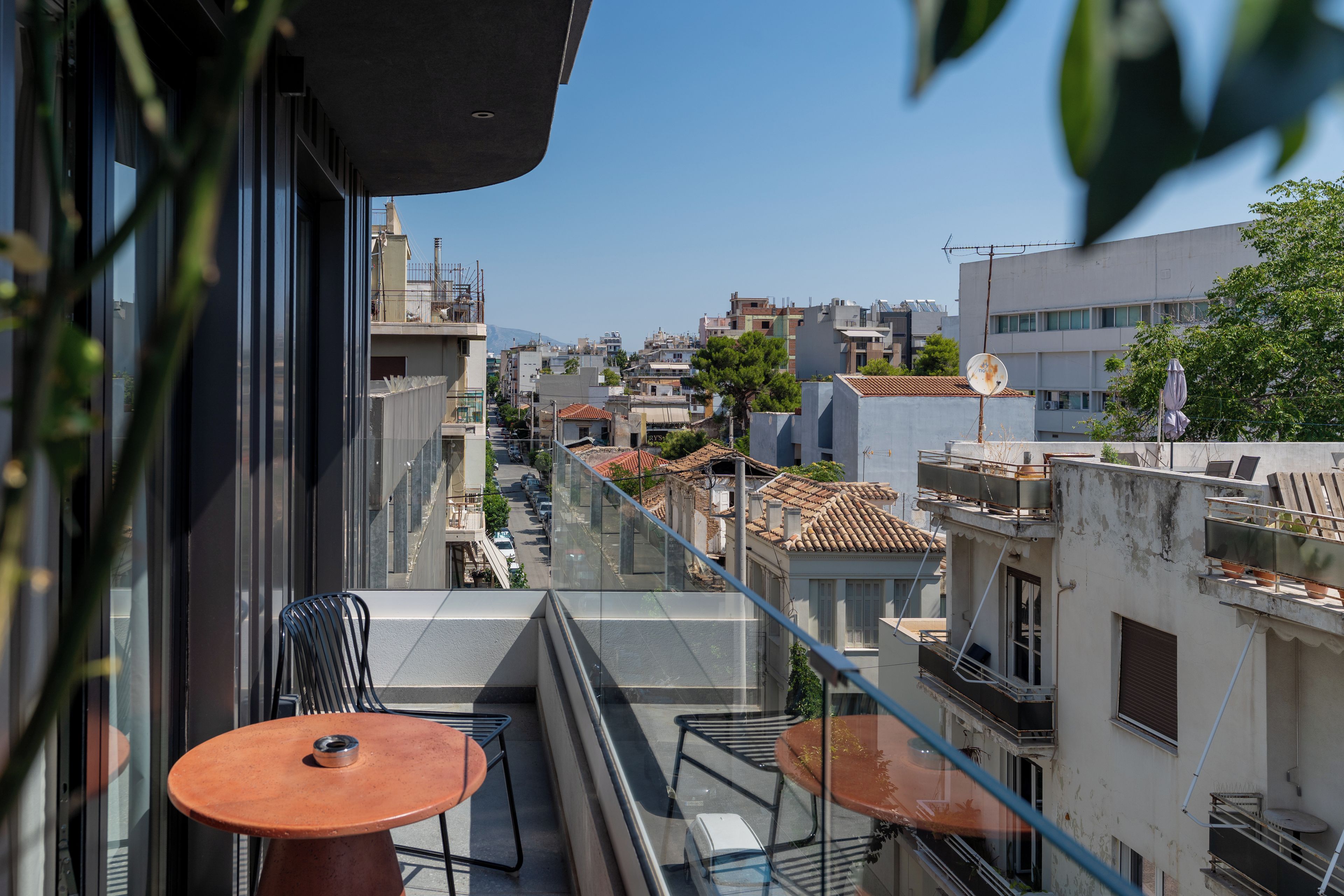 Ein Balkon mit Tisch und Stühlen, der auf einen Stadtblick mit Gebäuden und blauem Himmel blickt.