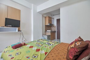 A bedroom with a bed, a TV mounted on the wall, and a kitchenette in the background. - Room Rendi @ Gunung Putri Square by Zuzu (Gunung Putri)