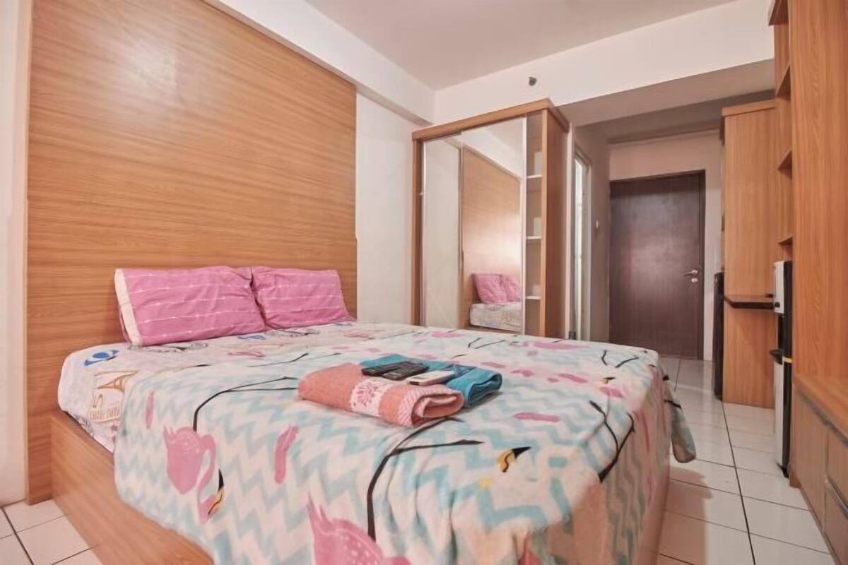 A bedroom with a bed, wooden headboard, a wardrobe, and a mirror.