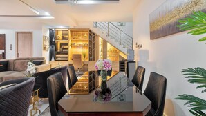 Un espace repas moderne avec une table en verre, des chaises noires et un vase de fleurs. Un escalier avec une rampe mène à un niveau supérieur.