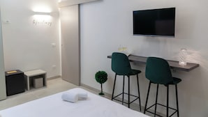 Una habitación de hotel moderna con una cama, un escritorio con dos sillas, un televisor de pantalla plana y una planta pequeña.