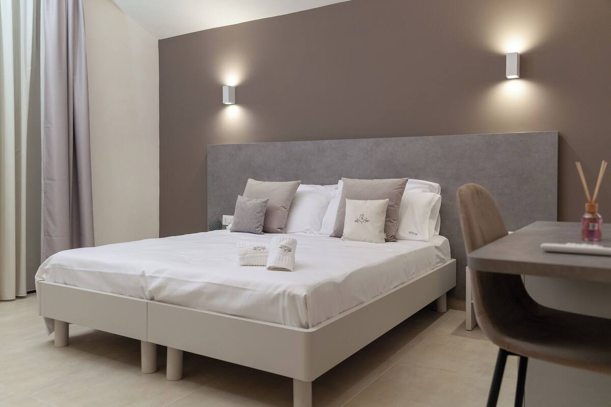 A modern bedroom with a large bed, bedside tables, and wall-mounted lights.