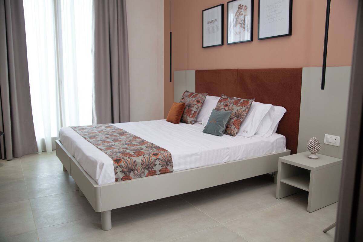 A modern bedroom with a large bed, a nightstand, and a wall-mounted shelf.