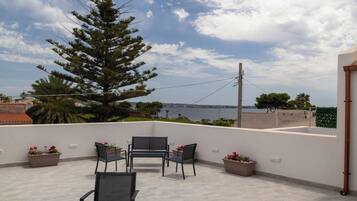 Una terraza con mobiliario exterior, un árbol grande y vistas al mar.