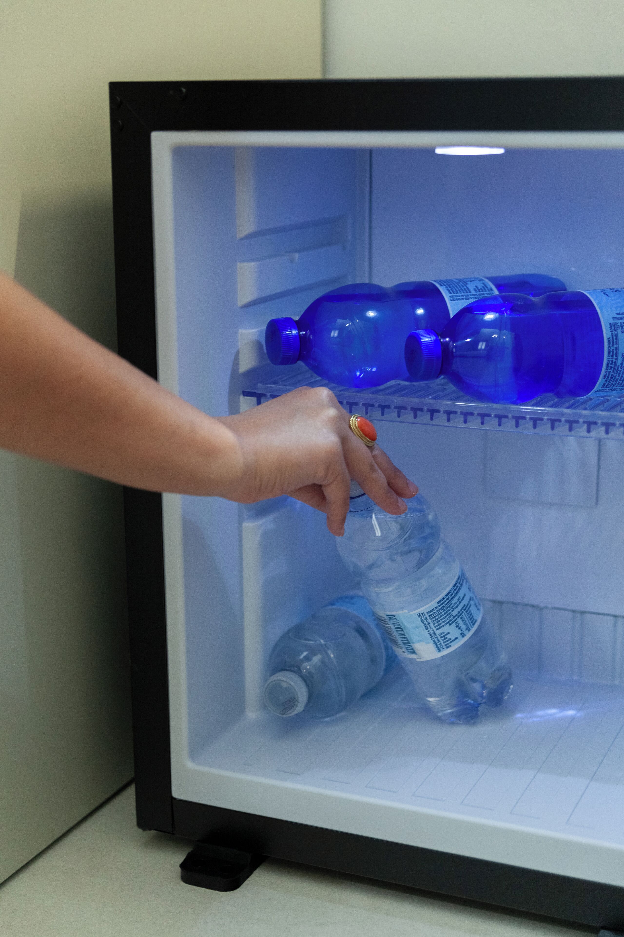 Une main dépose une bouteille d’eau dans un réfrigérateur à la structure noire et à l’intérieur blanc.