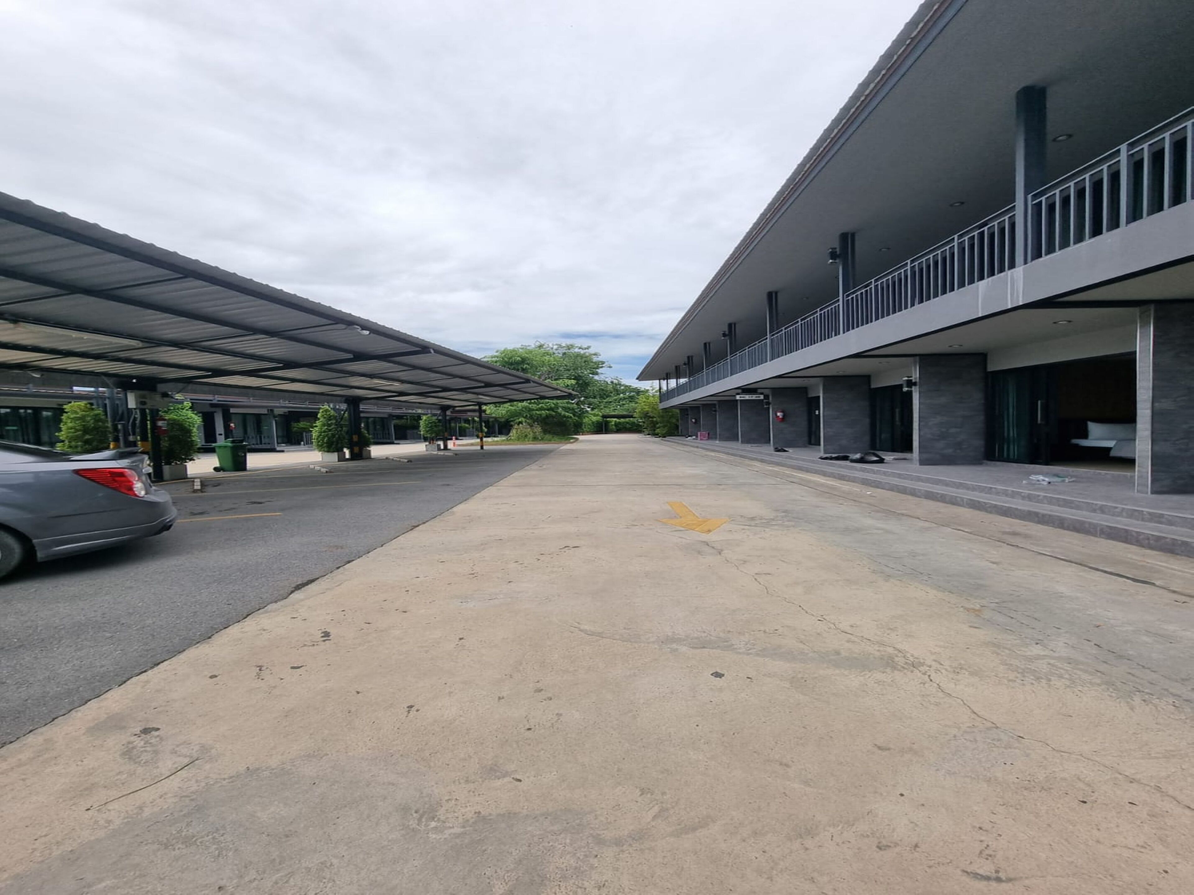 Un área de estacionamiento con un pasillo cubierto que conduce a un edificio de diseño moderno, con techo plano y balcón.
