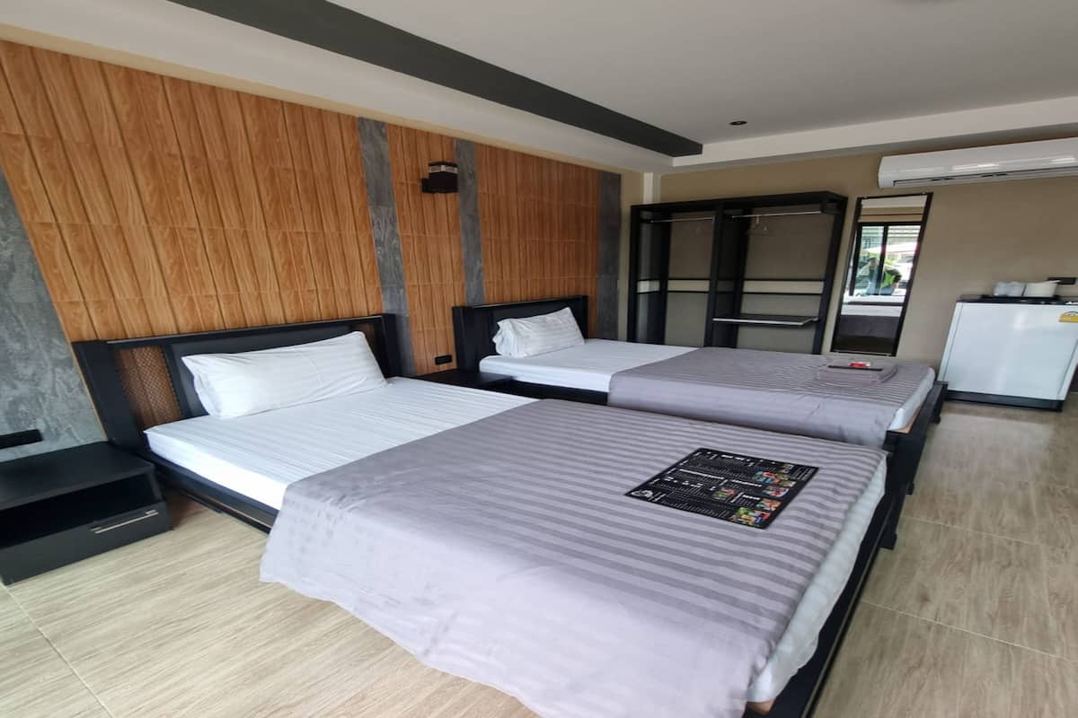 A hotel room with two beds, a small desk, a wardrobe, and an air conditioning unit.