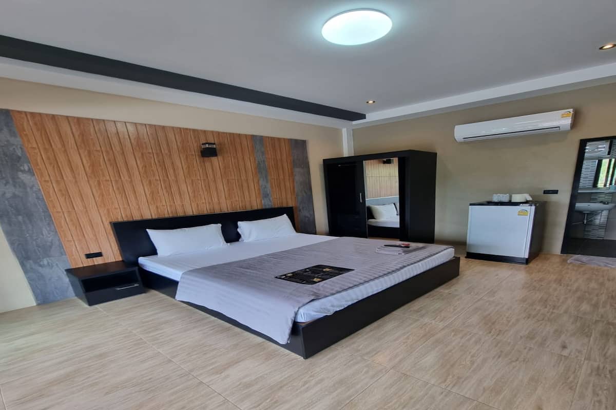 A modern hotel room with a large bed, a wardrobe, a small refrigerator, and an air conditioning unit.