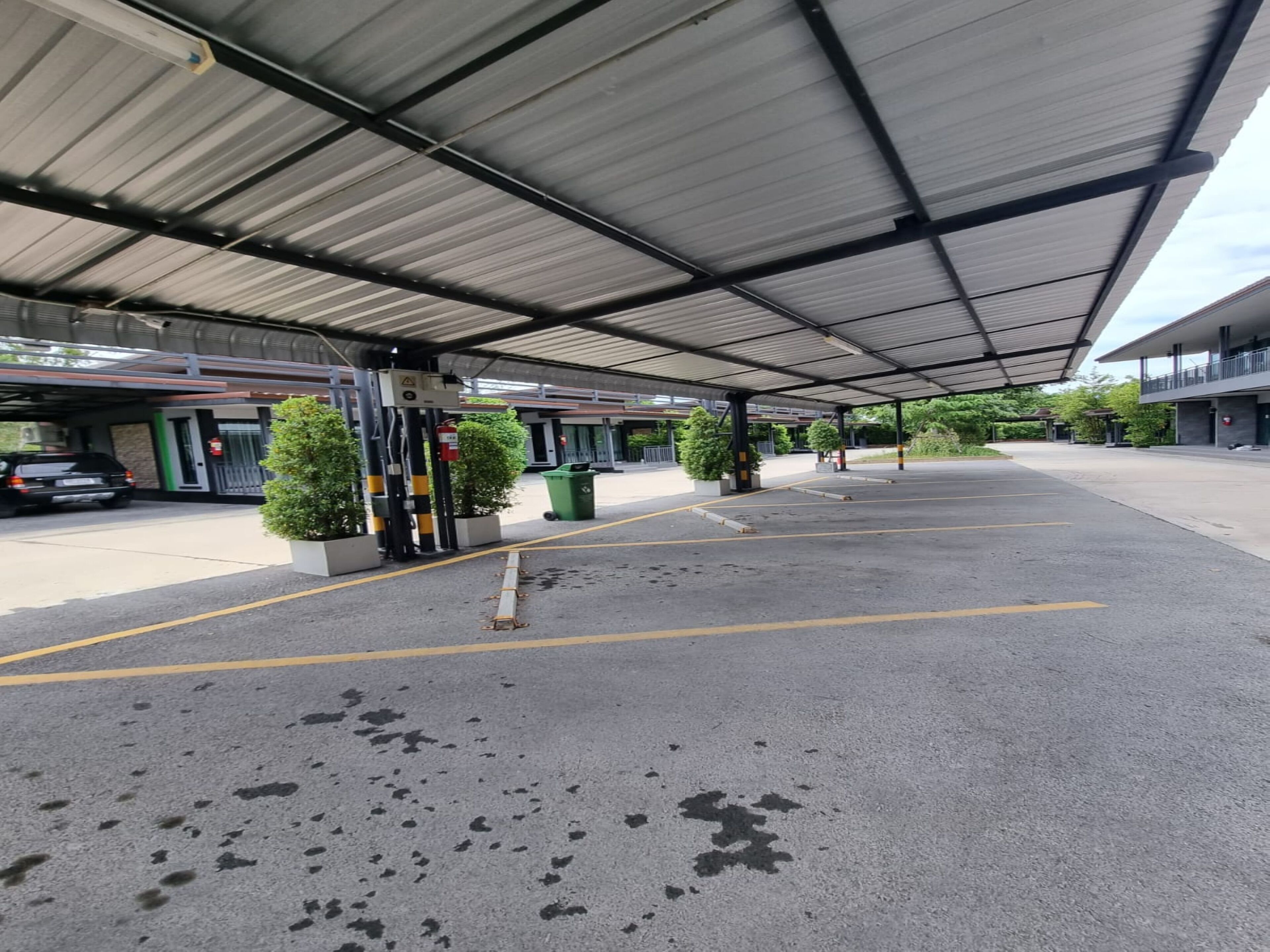 A covered parking area with a car and a trash bin.