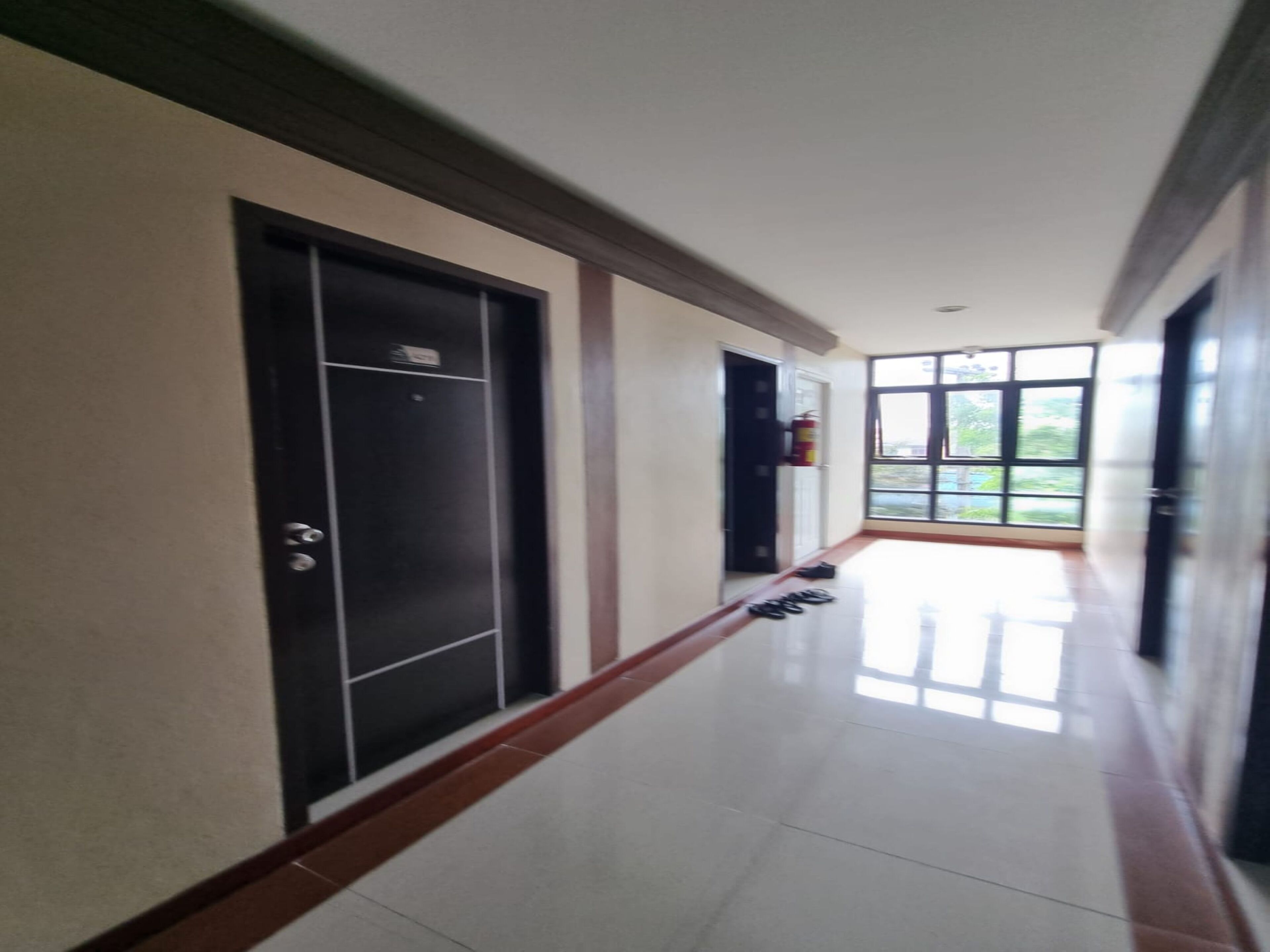 A hallway with a shiny tiled floor, black doors, and a fire extinguisher mounted on the wall.