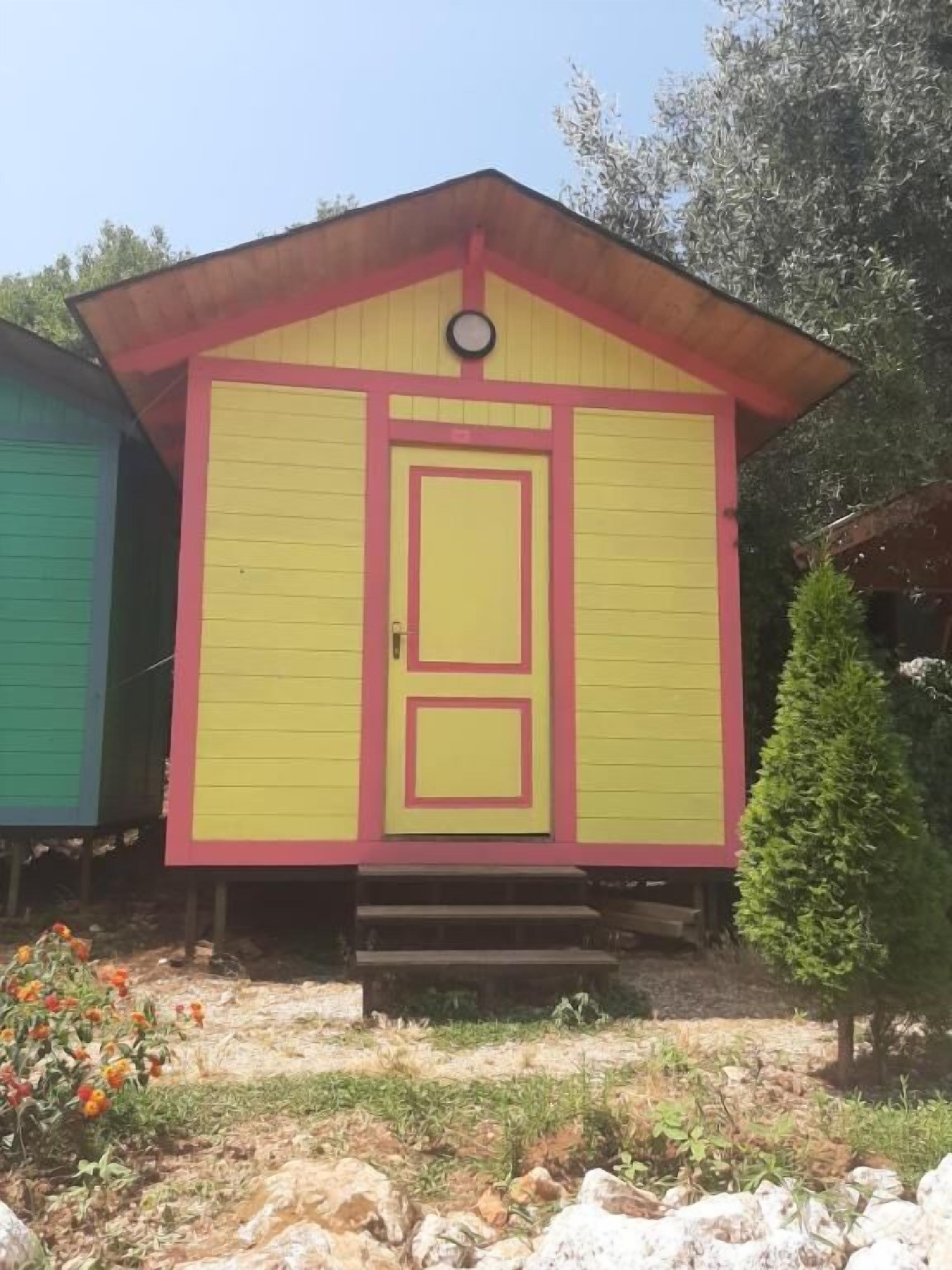 Ein kleines, einstöckiges Gebäude mit gelb-roter Fassade, einer mittleren Tür und einem kleinen, runden Fenster darüber.