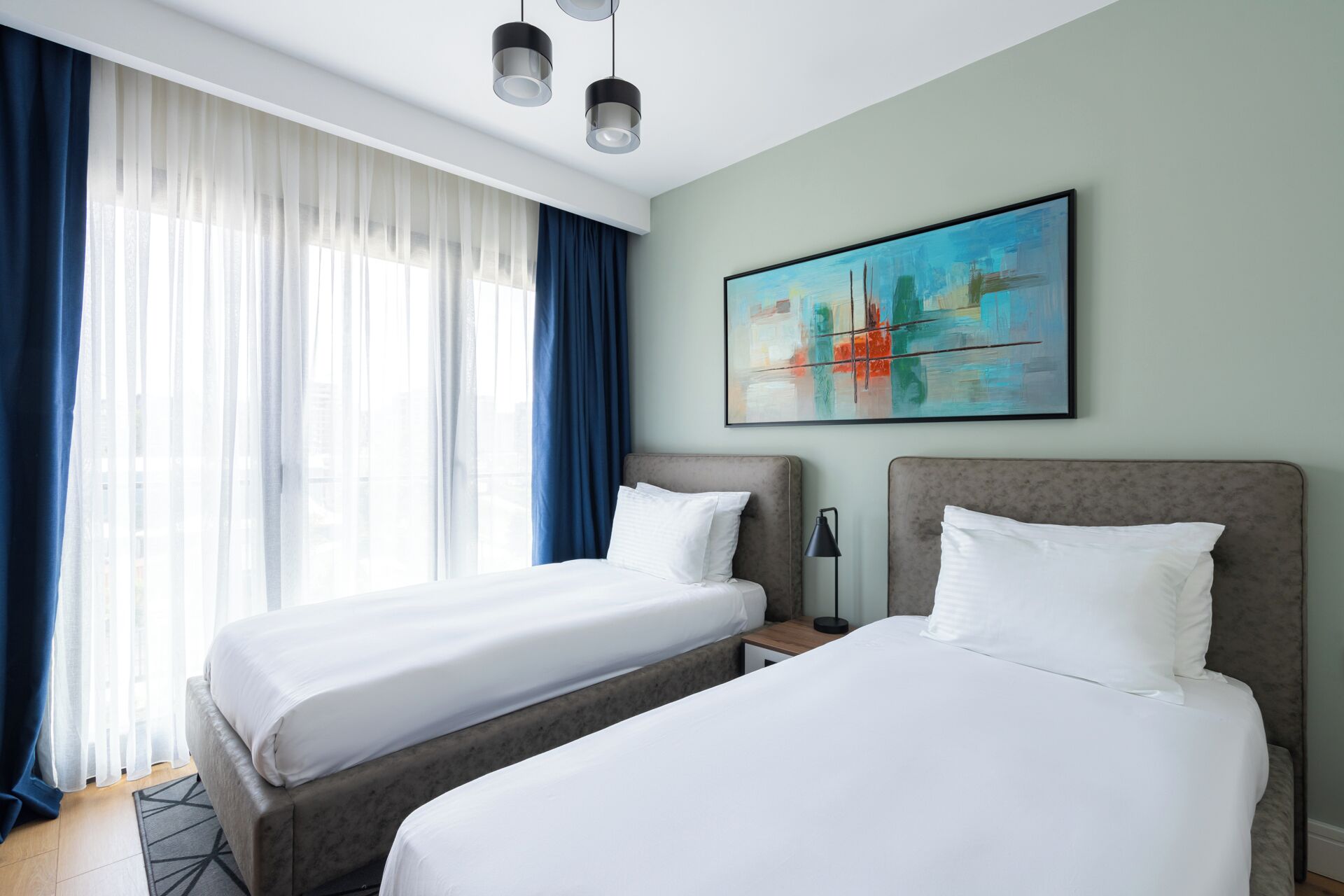 Ett hotellrum med två sängar, en tavla på väggen och ett fönster med gardiner.