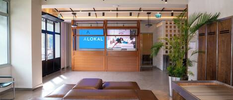 Eine moderne Lobby mit Ledersitzgelegenheiten, einem Empfangstresen und einem großen ALOKAL-Schild.