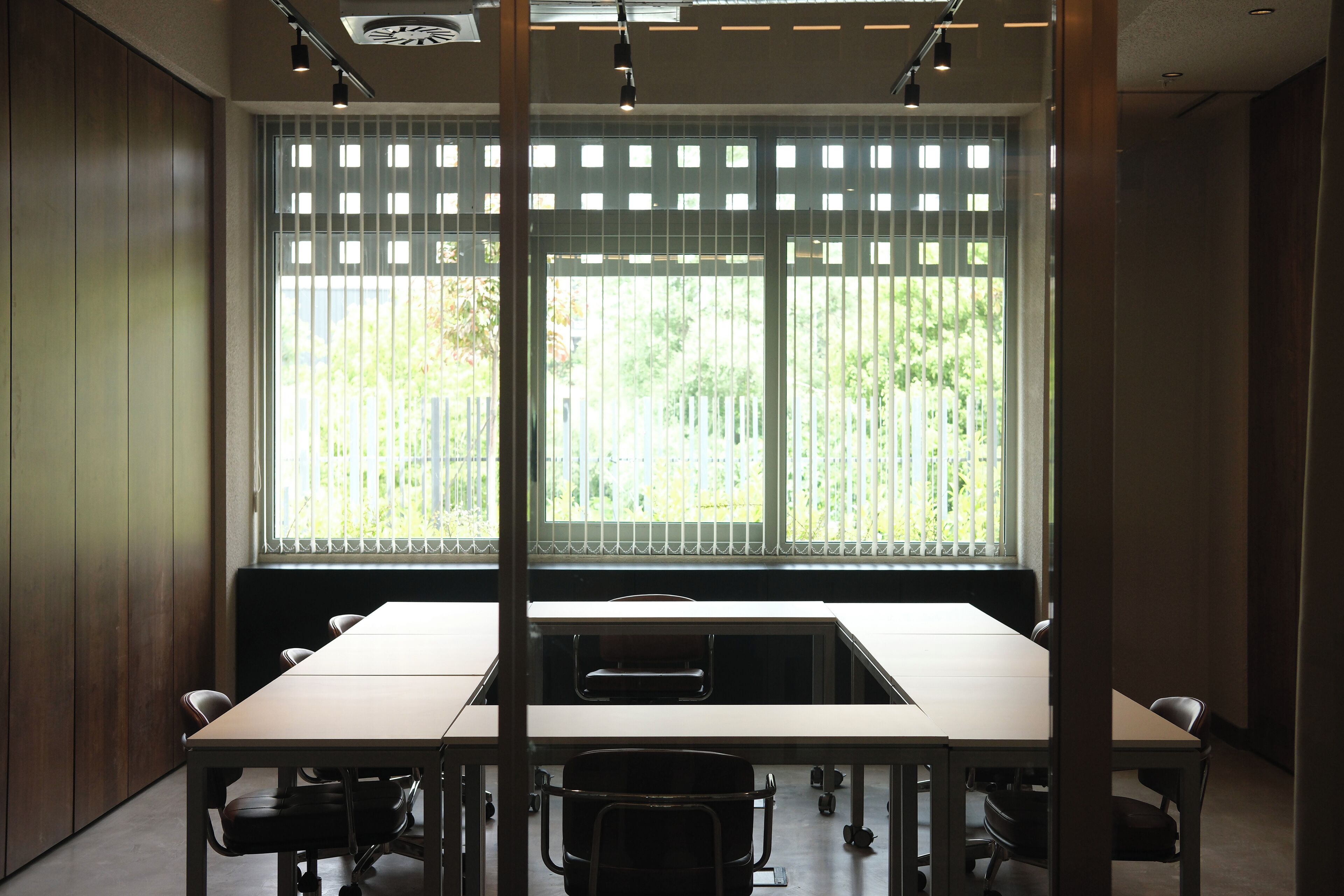 A conference room with a long table, chairs, and a view through a window with blinds.