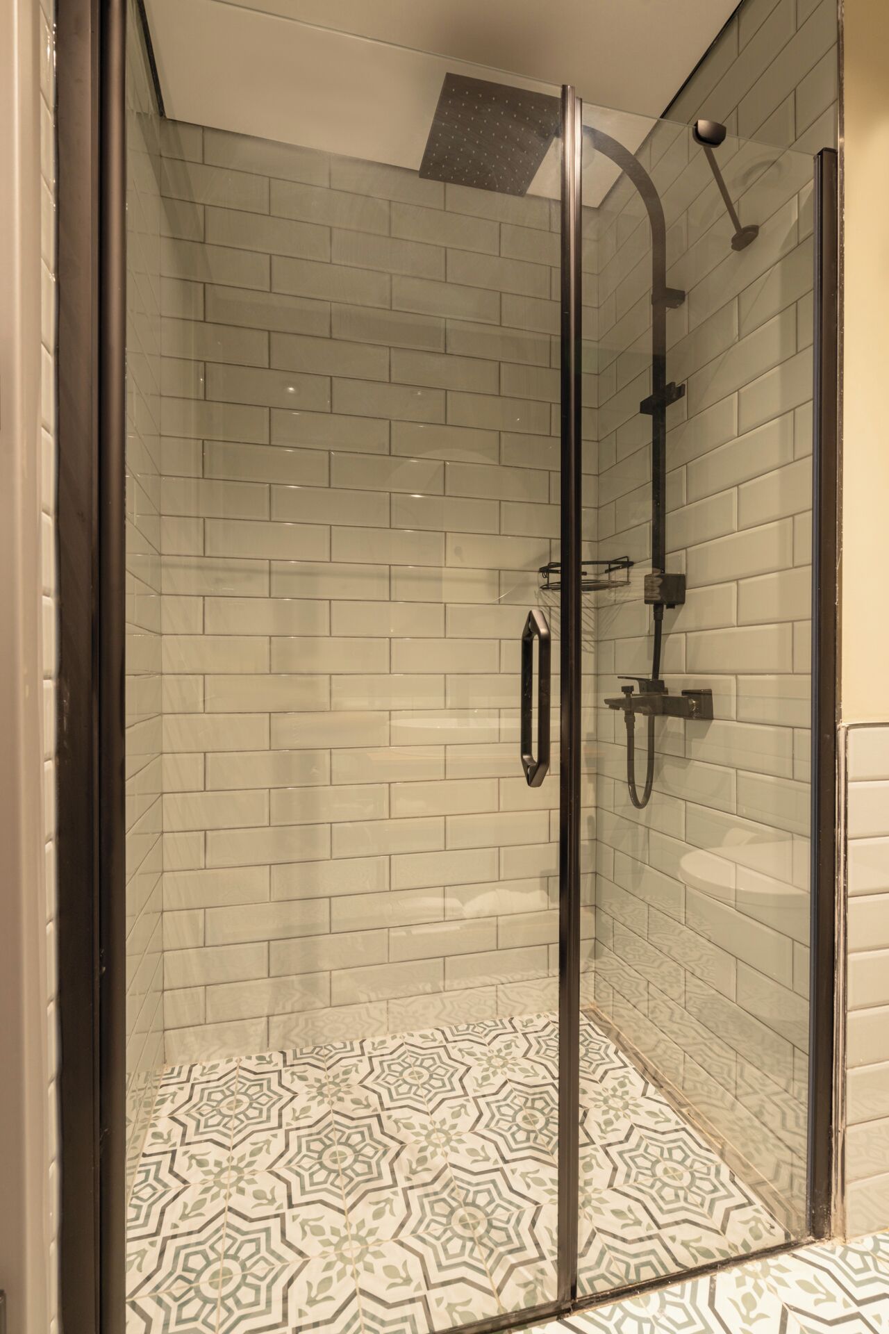 A glass-enclosed shower with a tiled floor and walls, a handheld showerhead, and a wall-mounted faucet.