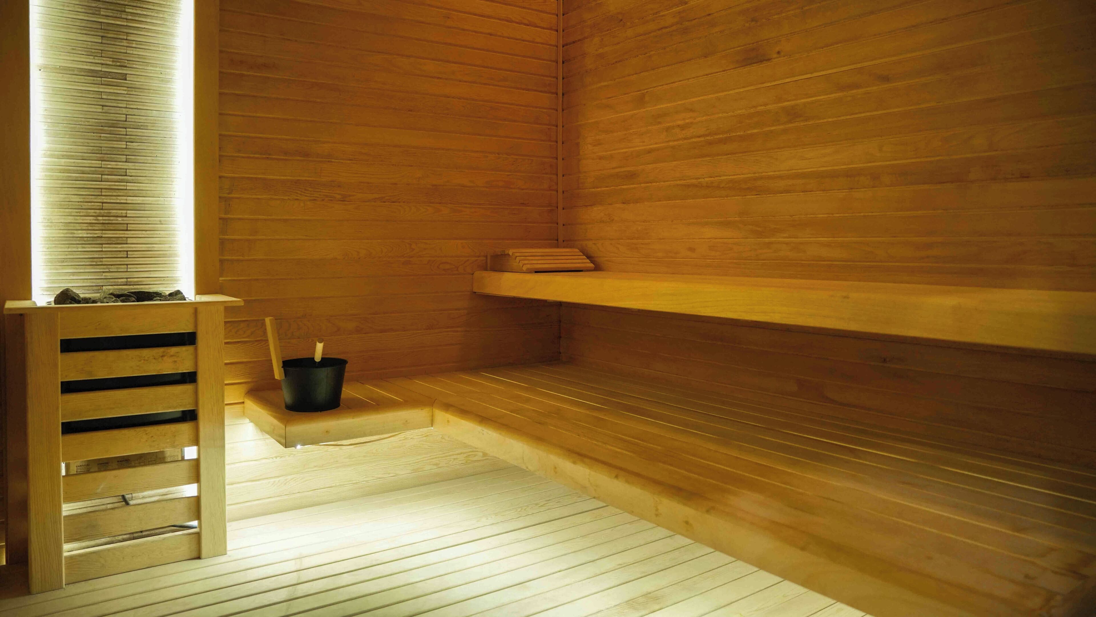 A wooden sauna with benches, a shelf, and a bucket.