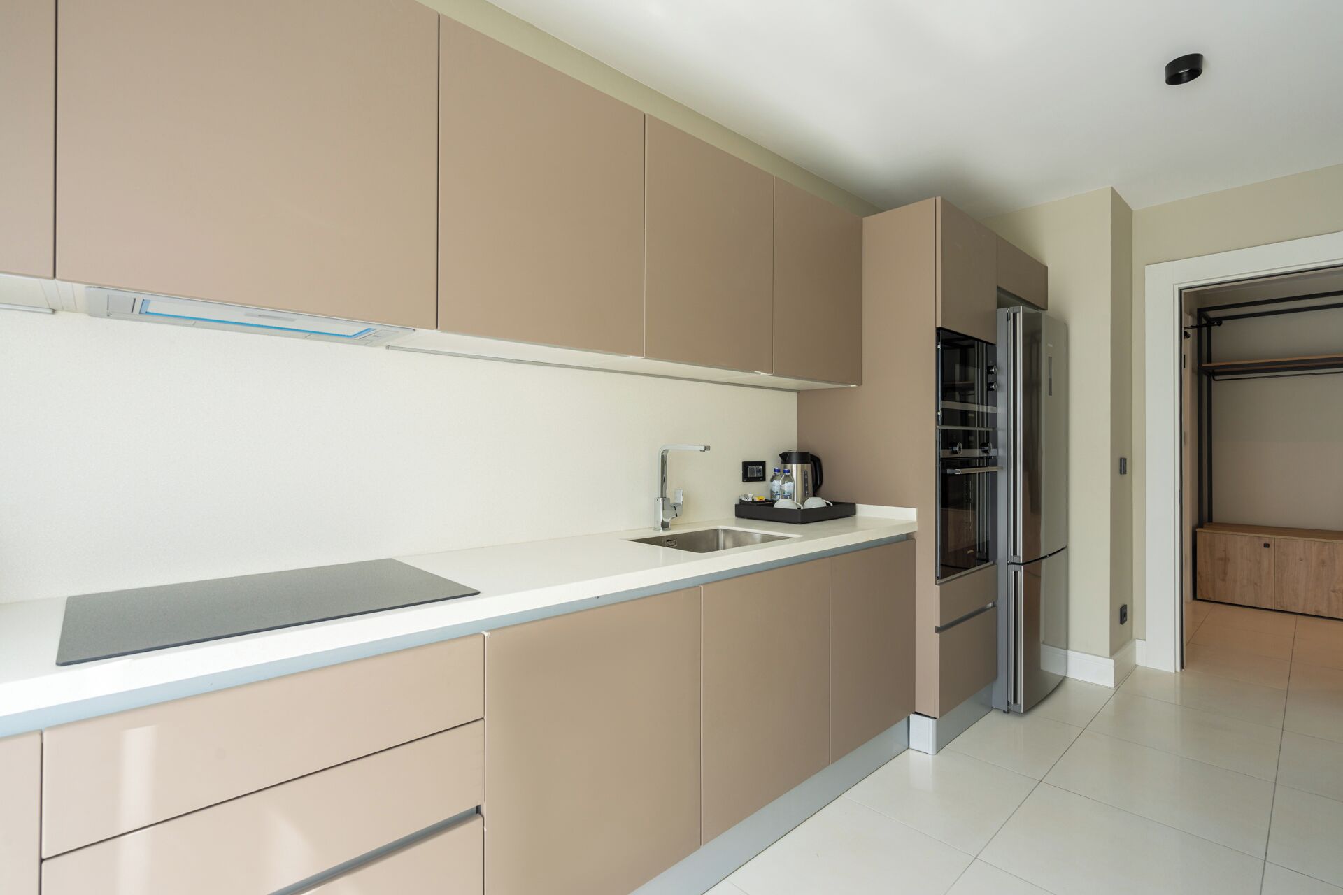 A modern kitchen with beige cabinets, a stainless steel refrigerator, and a white countertop.
